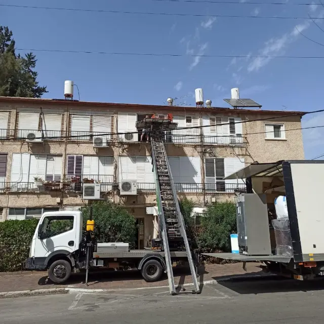 משאית המנוף של מנופי מיה לגובה בהרמה לבניין מגורים, משאית הובלה לידה